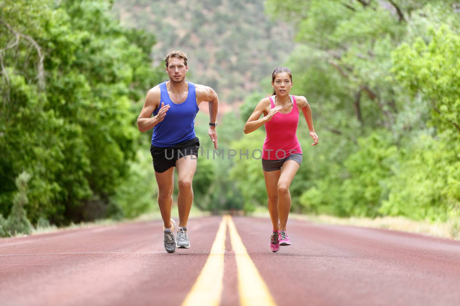 Determined Athletes Running On Road Against Trees by Maridav