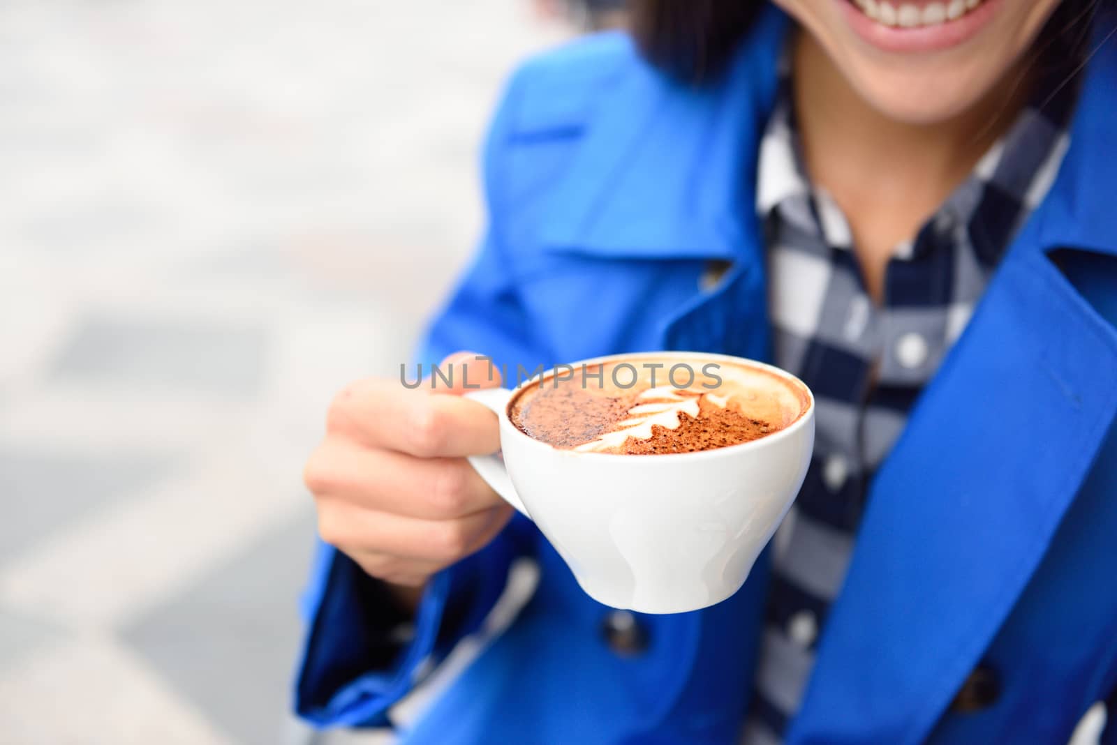 Hands closeup of woman drinking at cafe holding a coffee cup with a milk rosetta foam shape on top. Outdoor terrace at coffee shop or restaurant. by Maridav