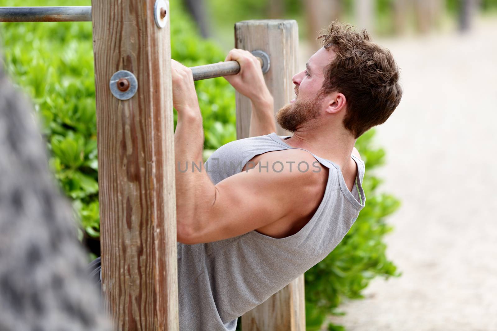 Pull-up strength training exercise - fitness man working out his arm muscles on outdoor beach gym doing chin-ups / pull-ups as part of a crossfit workout routine. by Maridav