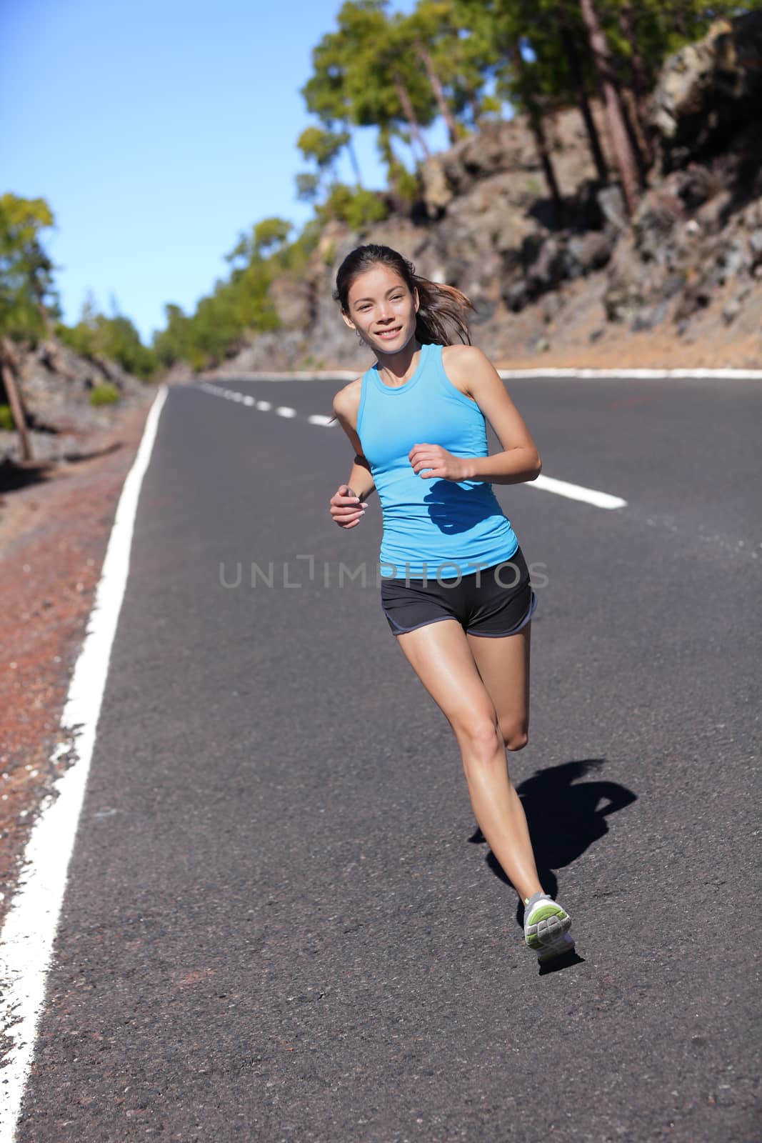 Female road runner training running in outdoor nature. Asian woman jogging fast working out her cardio in blue top and black shorts activewear.