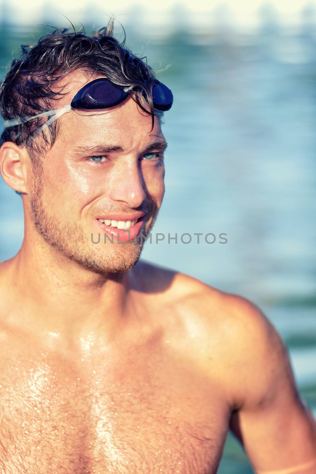 Athlete swimmer in swimming pool with swim goggles. Handsome young professional male sports adult portrait looking happy after cardio workout exercising in outdoor water, topless wearing swimwear.