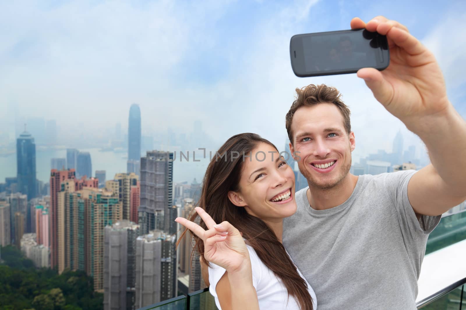 Multiethnic Chinese Caucasian couple in Hong Kong. Young people taking a smartphone selfie picture at viewpoint of famous attraction Victoria Peak, HK, China. Young multiracial group of people.