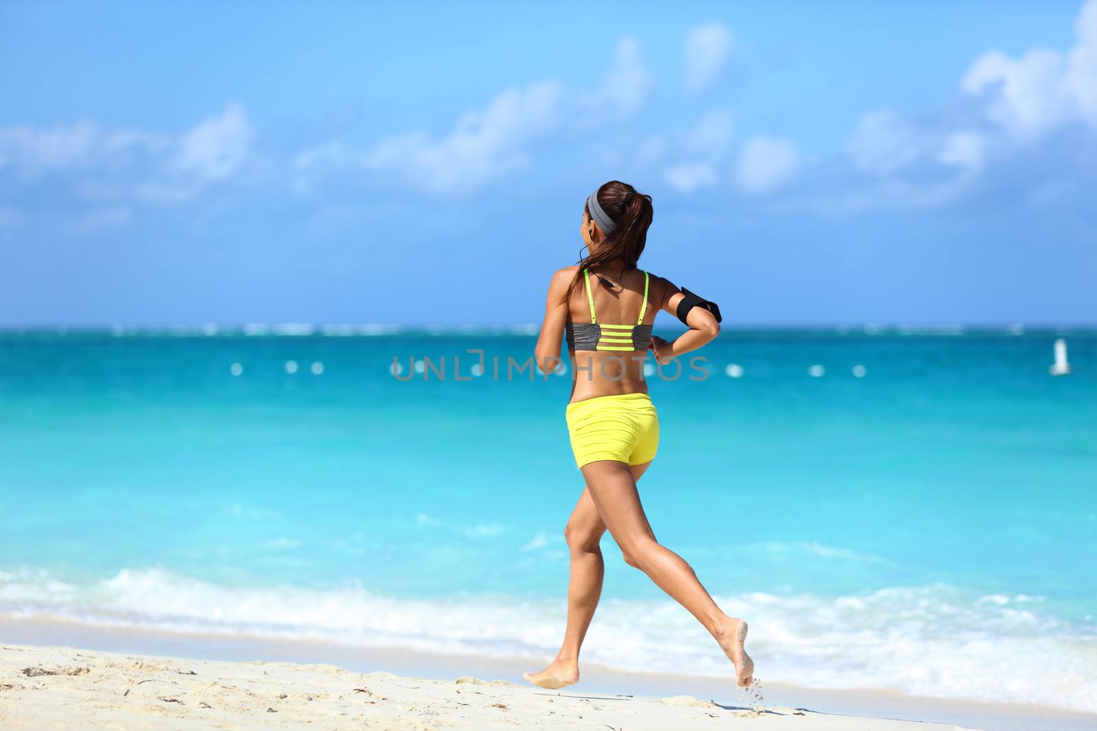 Running on beach - summer workout active lifestyle. Female athlete from the back running away barefoot on the sand in trendy activewear outfit training cardio for weight loss.