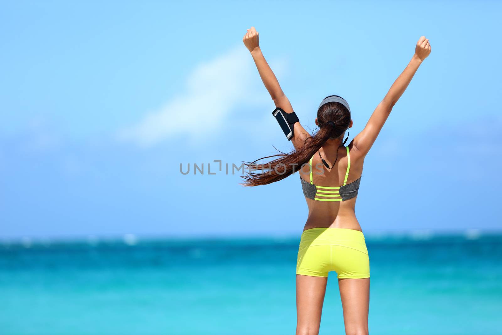 Success fitness woman concept with sports armband and earphones. Winning concept of female athlete runner cheering with arms raised up for achievement in weight loss or life goal.