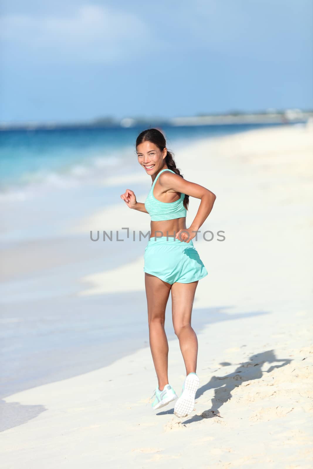 Happy healthy lifestyle woman runner looking back running on beach by Maridav