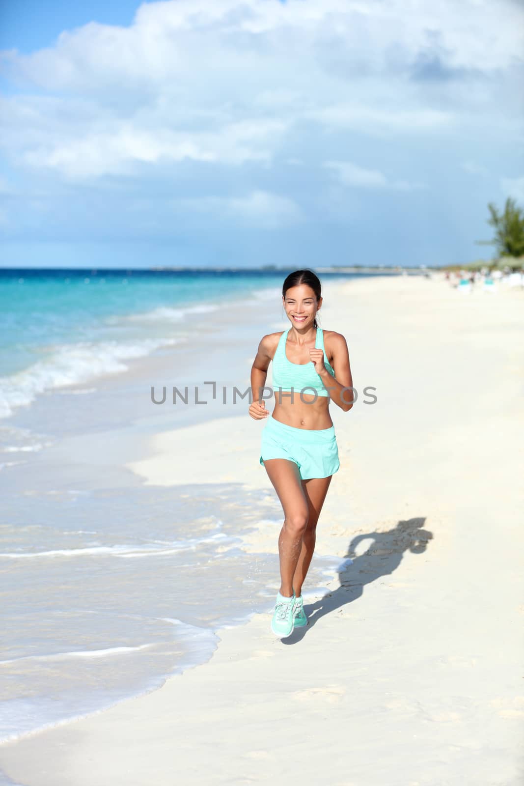 Happy jogging woman running on sunny beach living a fit and active life. Happiness and health concept on summer vacation travel beach.