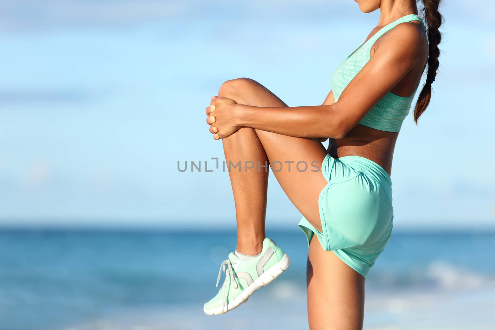 Runner stretching leg during outdoor warm-up on beach before run by Maridav