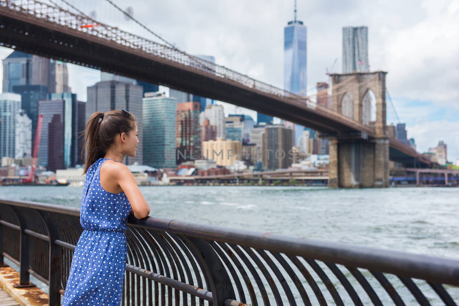 New York city urban woman enjoying view of Brooklyn bridge and NYC skyline living a happy lifestyle walking during summer travel in USA. Female Asian tourist in her 20s.