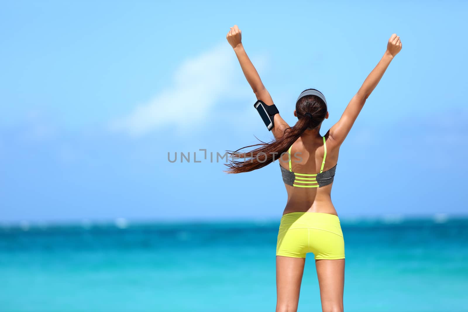 Strong fitness athlete arms up in success on summer beach after cardio training workout. Female runner woman running winning reaching goal achievement during strength training showing power.