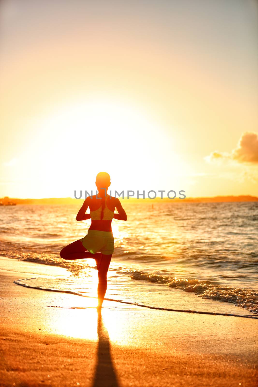 Yoga fitness woman practicing tree pose on beach at sunset by Maridav