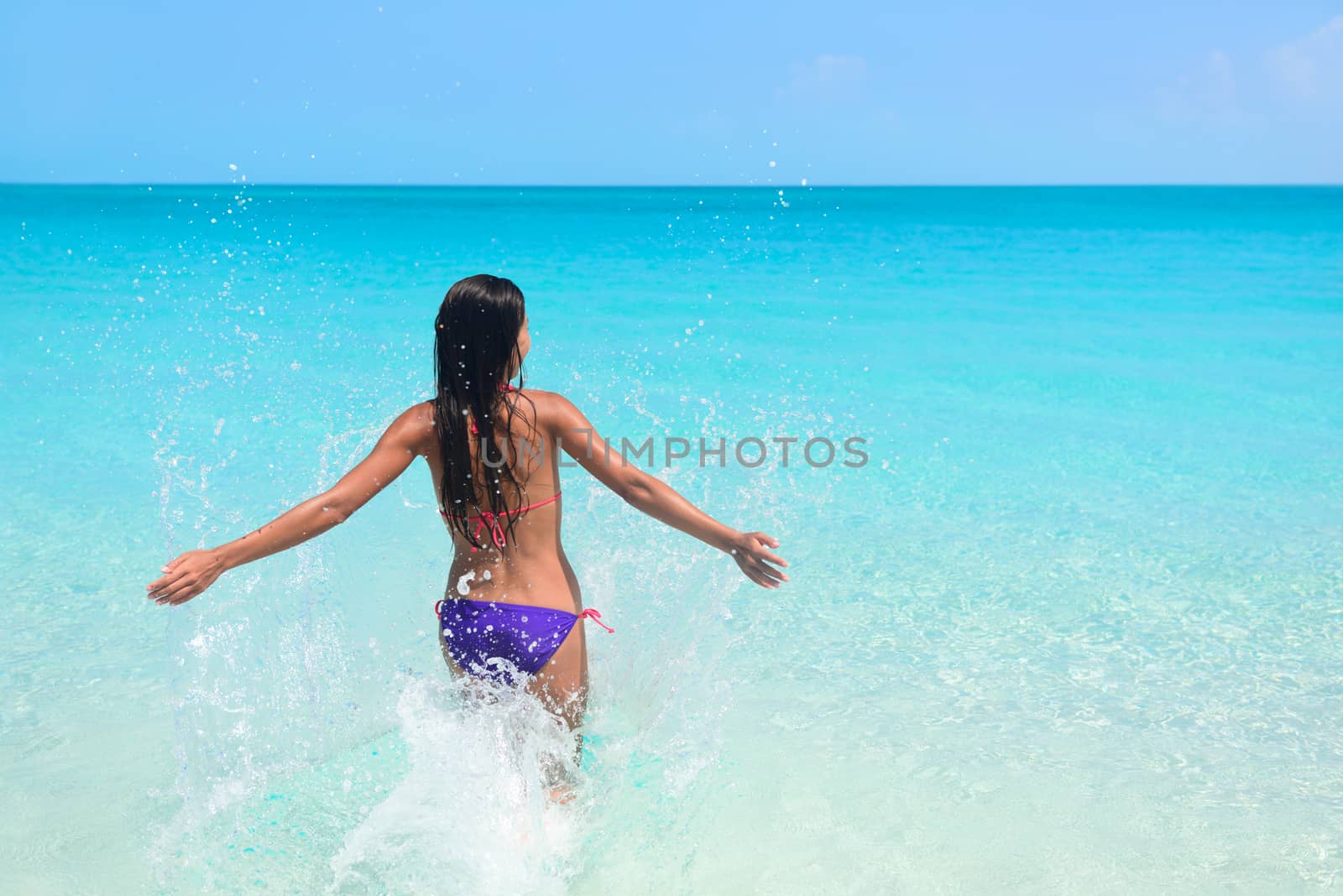 Young woman enjoying herself in sea during summer holidays. Exhilarated female is in bikini. Tourist with arms outstretched is on her vacation at beach.