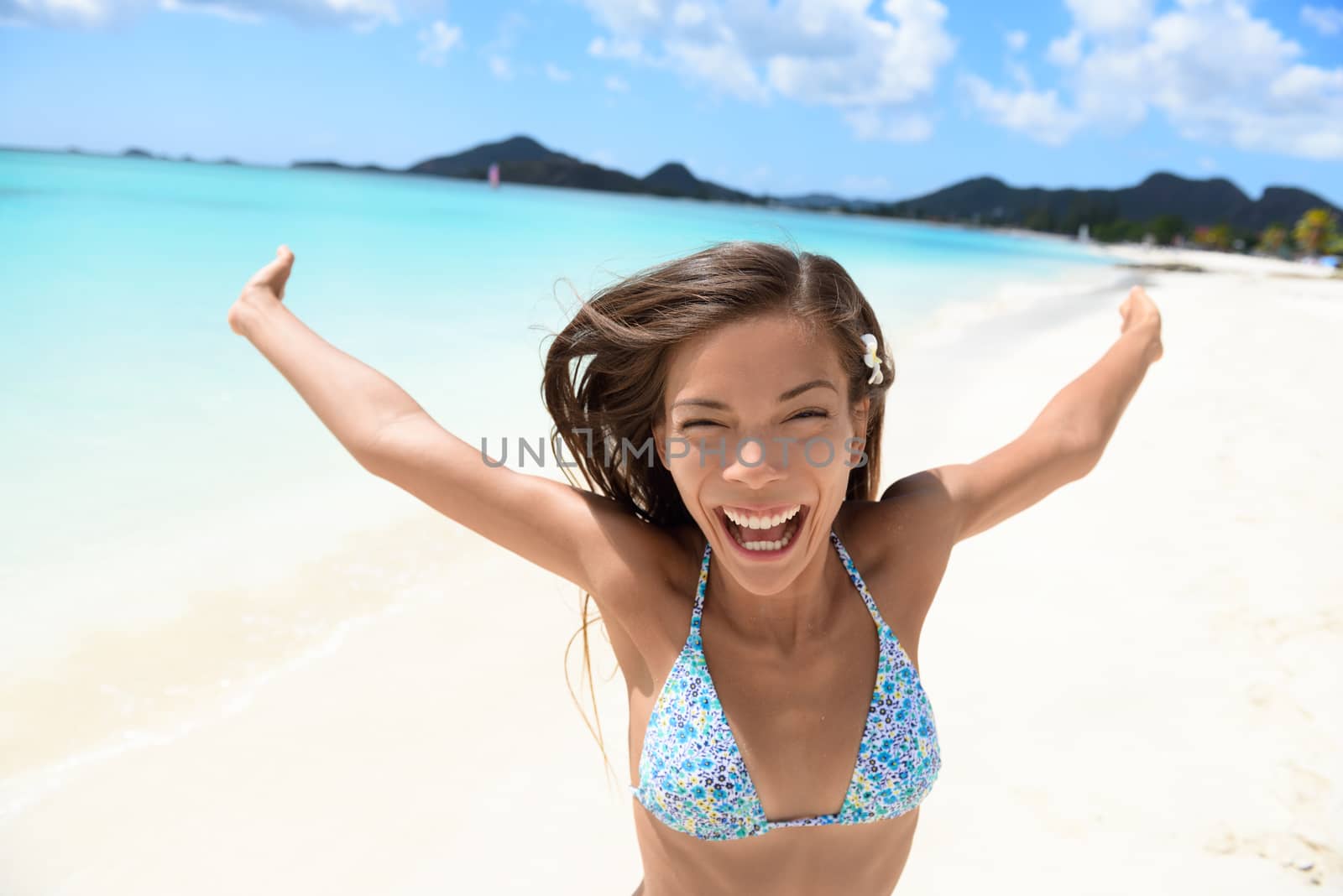 Exhilarated young woman screaming on beach. Portrait of cheerful female in bikini enjoying her summer vacation. Attractive tourist is standing with arms outstretched in nature.