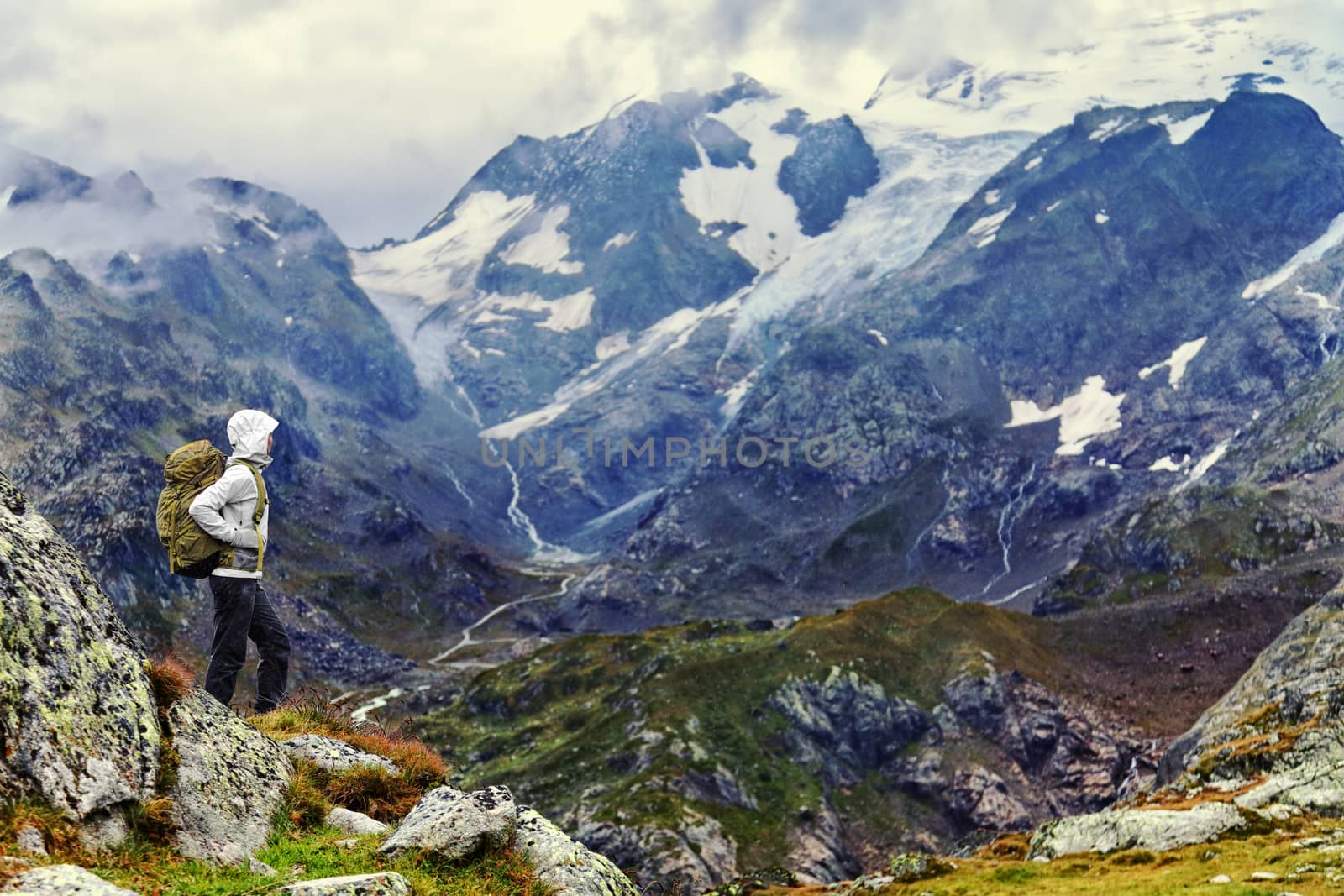 Female hiker standing on mountain on hiking trek. Side view of woman in warm clothing carrying backpack. Woman is enjoying idyllic view of mountain range.