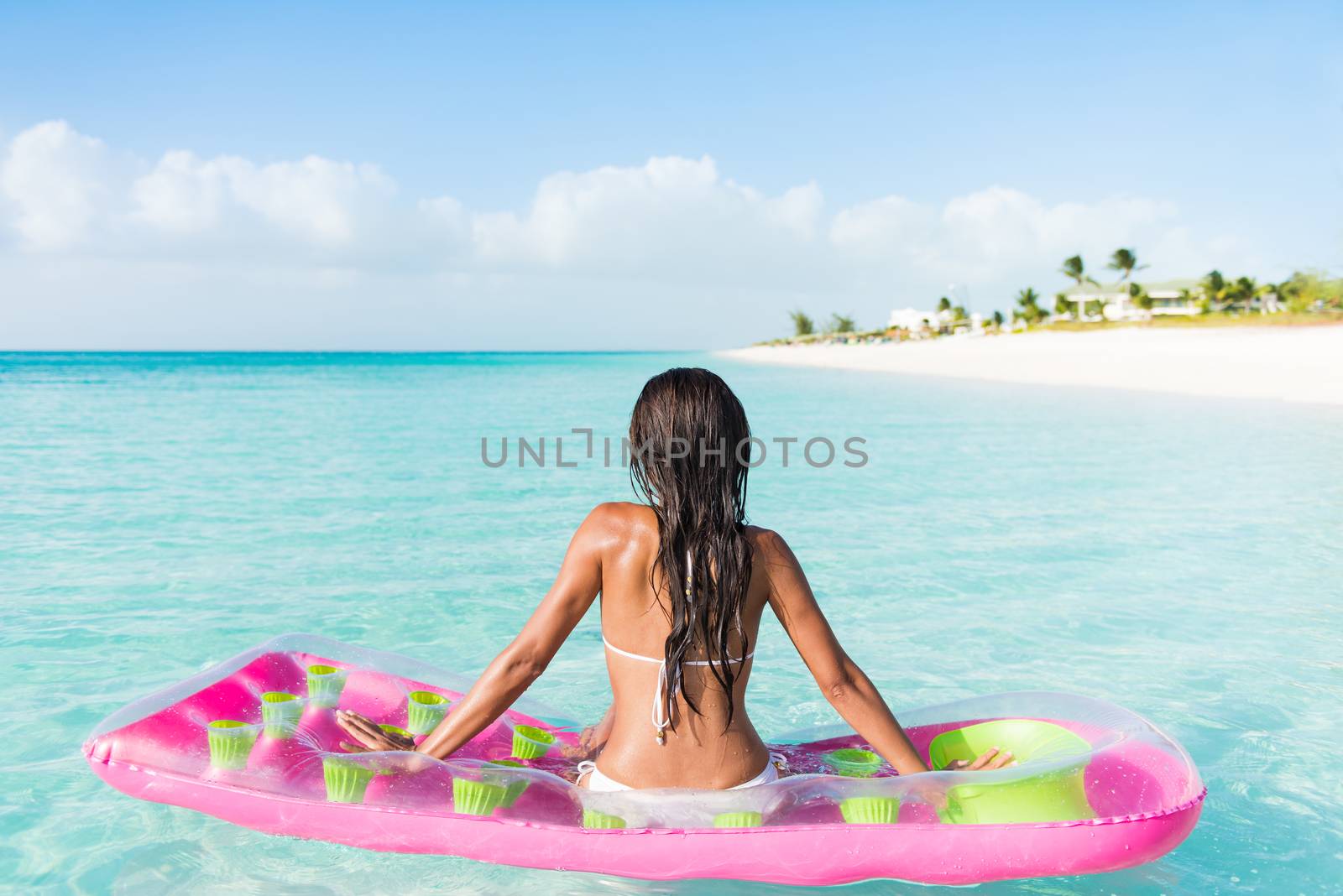 Beach relaxation woman floating on pink inflatable air bed pool mattress toy float in ocean beach background in pristine blue turquoise water at luxury caribbean getaway resort.