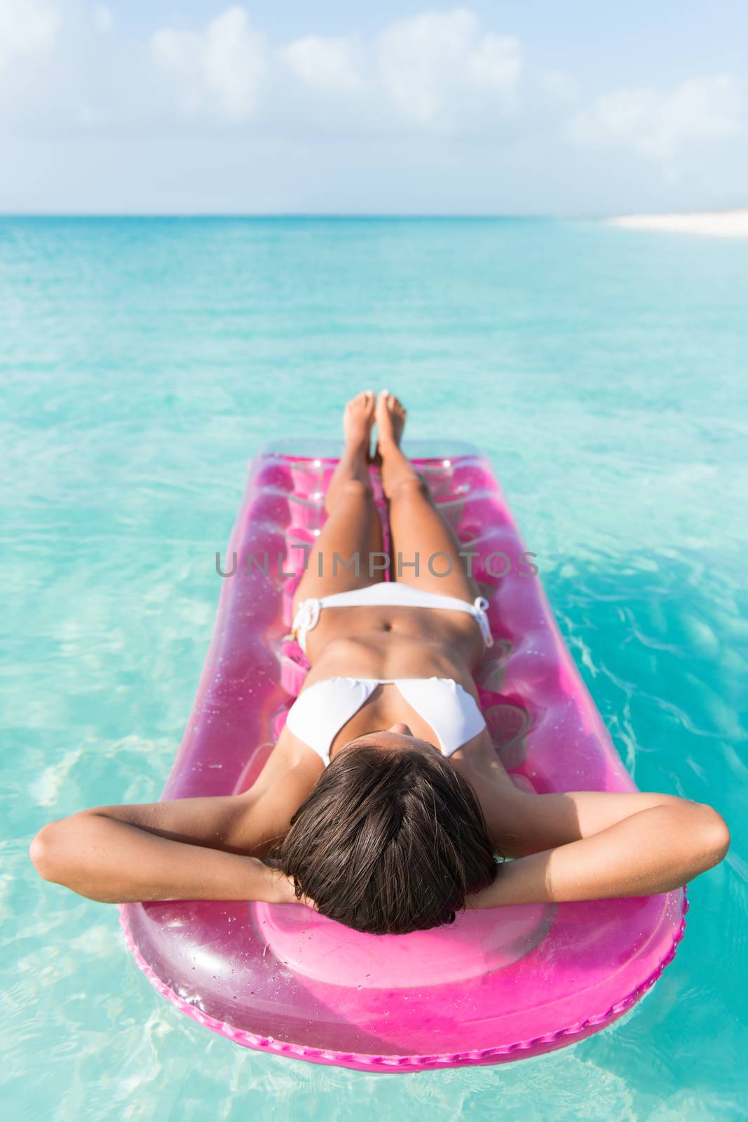 Beach vacation woman relaxing in pink plastic pool toy air bed float floating on ocean water on tropical vacation seen from above lying down lounging and sunbathing.