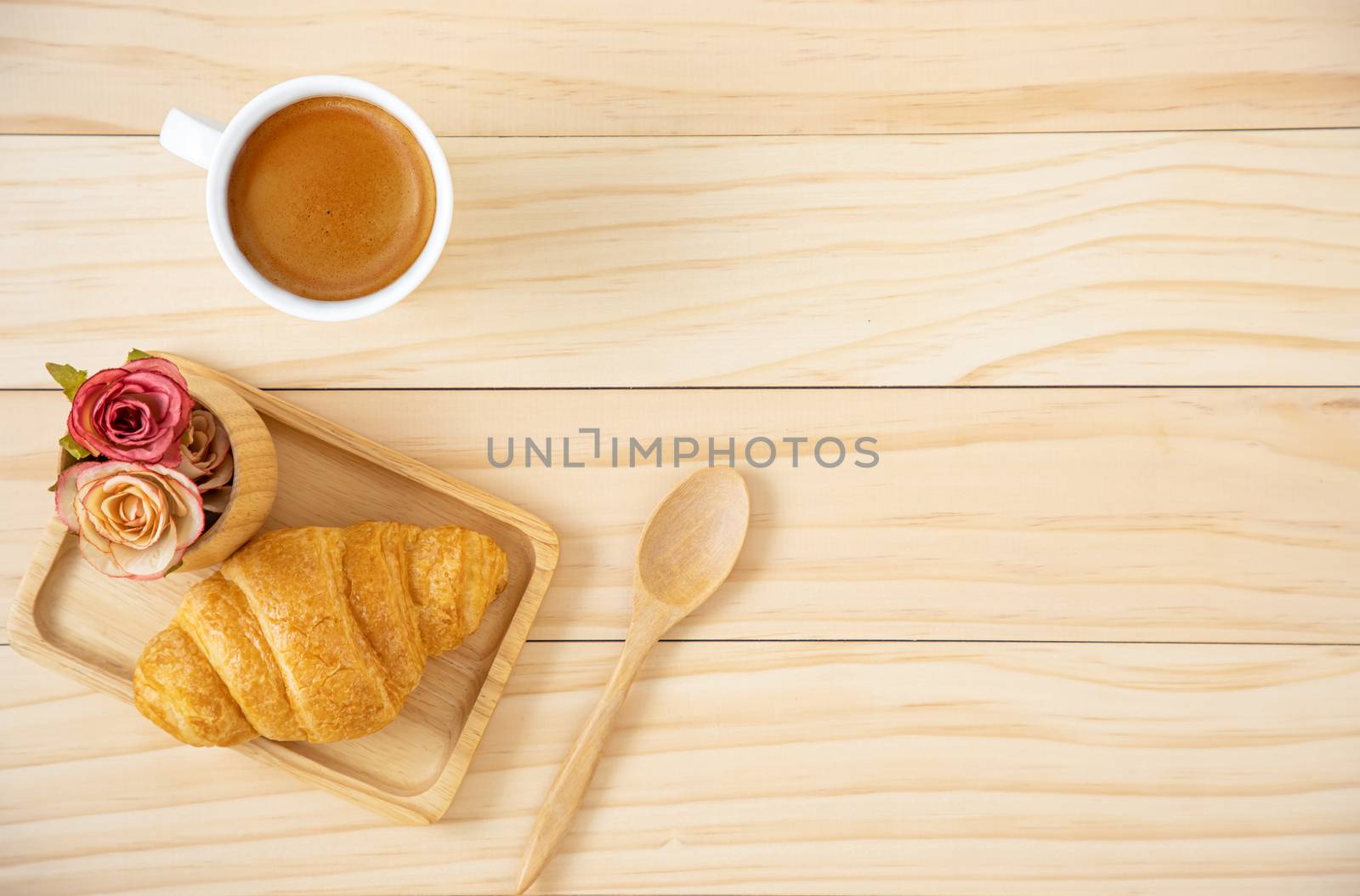 A piece of butter croissant on a squate wooden plate and a cup of coffee in white ceramic mug. Wooden background.