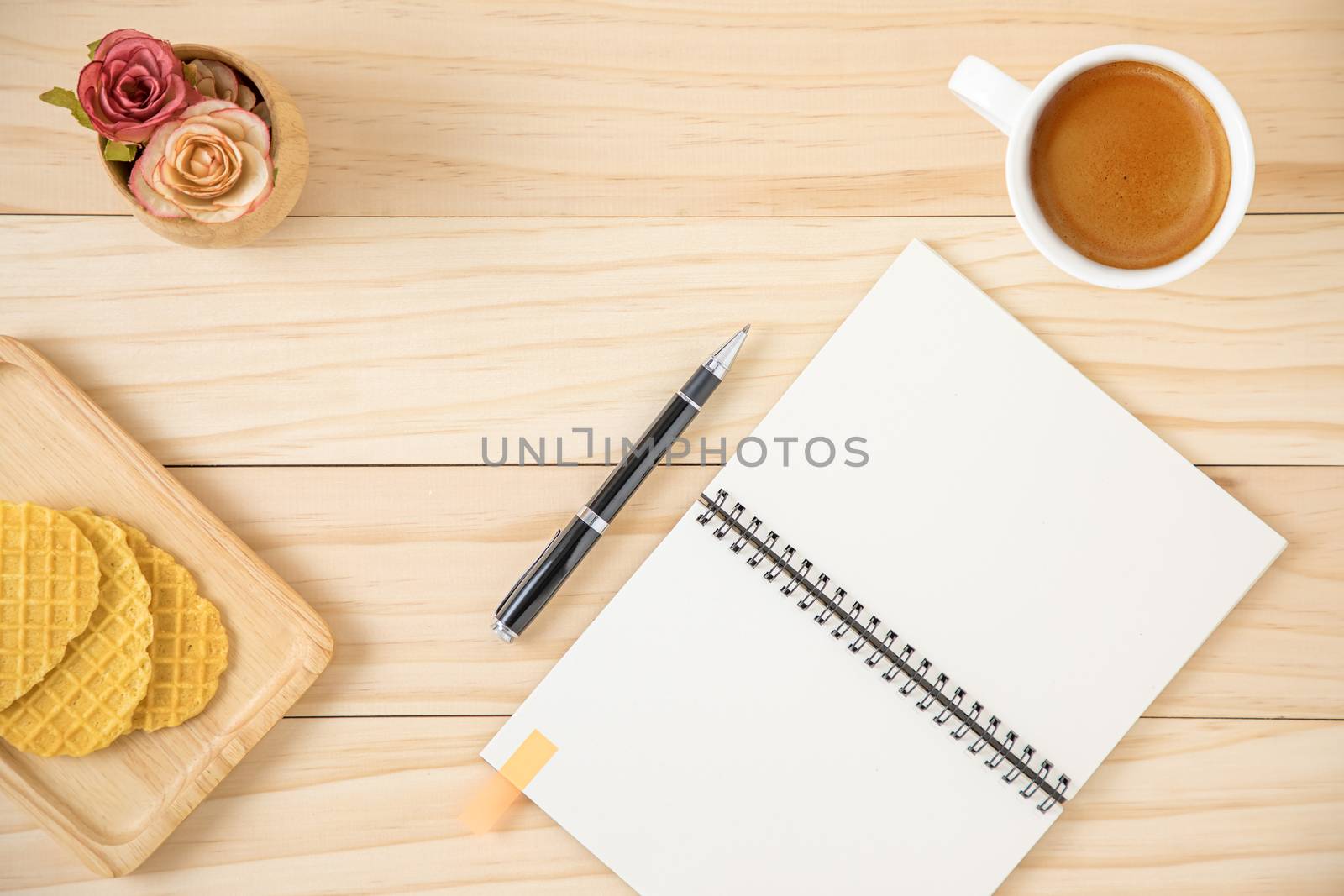 A blank notebook and a cup of coffee in white ceramic cup. Wooden background.