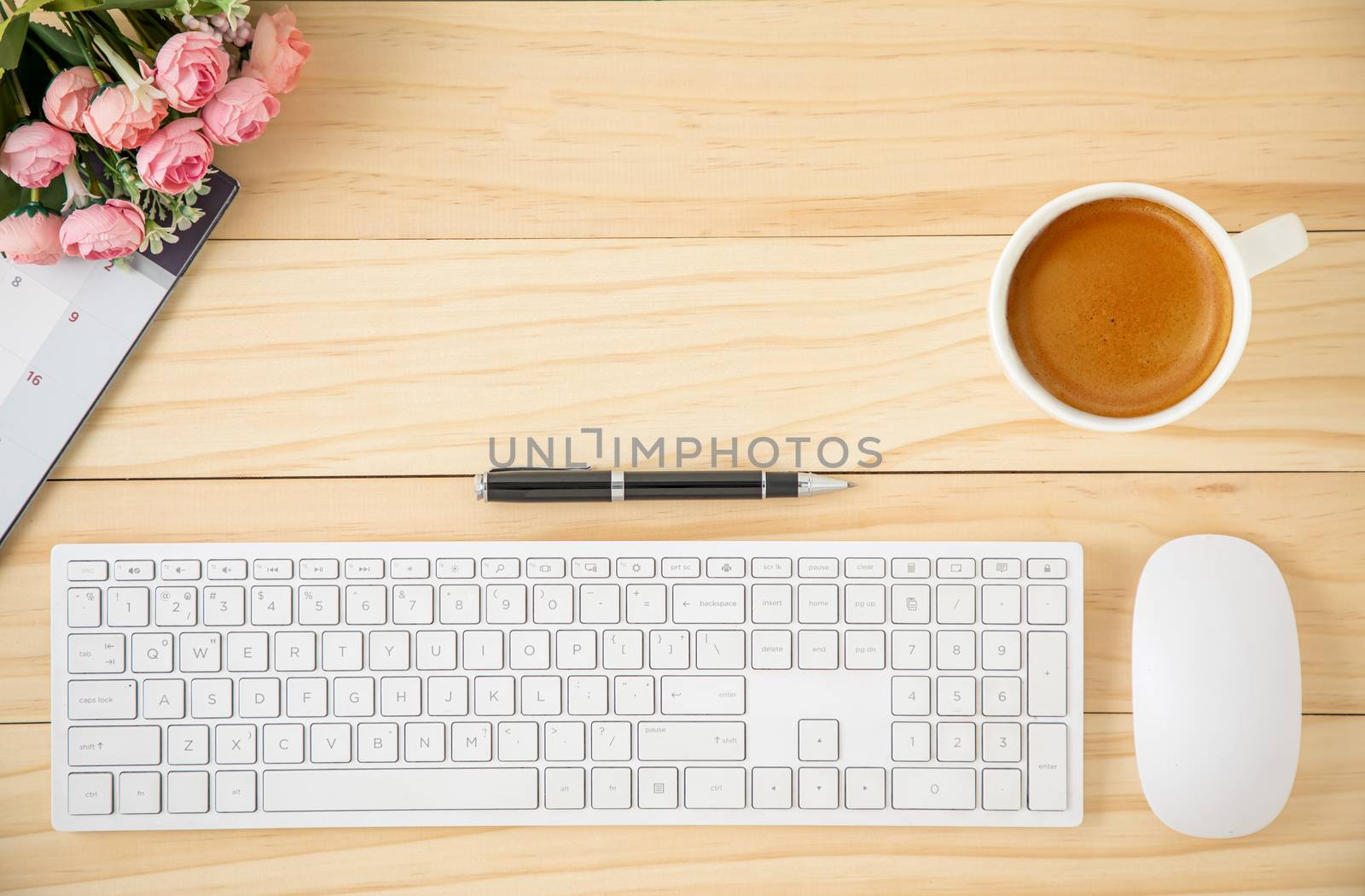 A minimal business workspace with white wireless computer mouse and keyboard with coffee in a white ceramic cup.