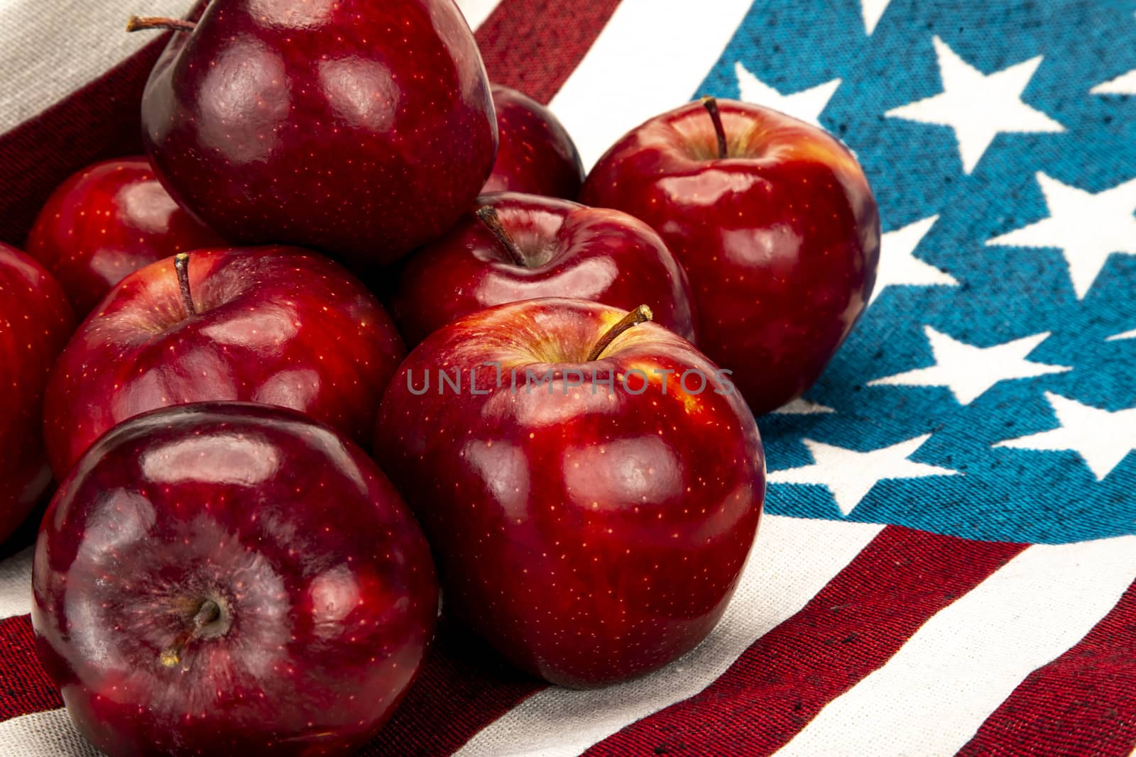 Pile of red apples on a cotton cloth with white stars on blue background and red and white stripes pattern.