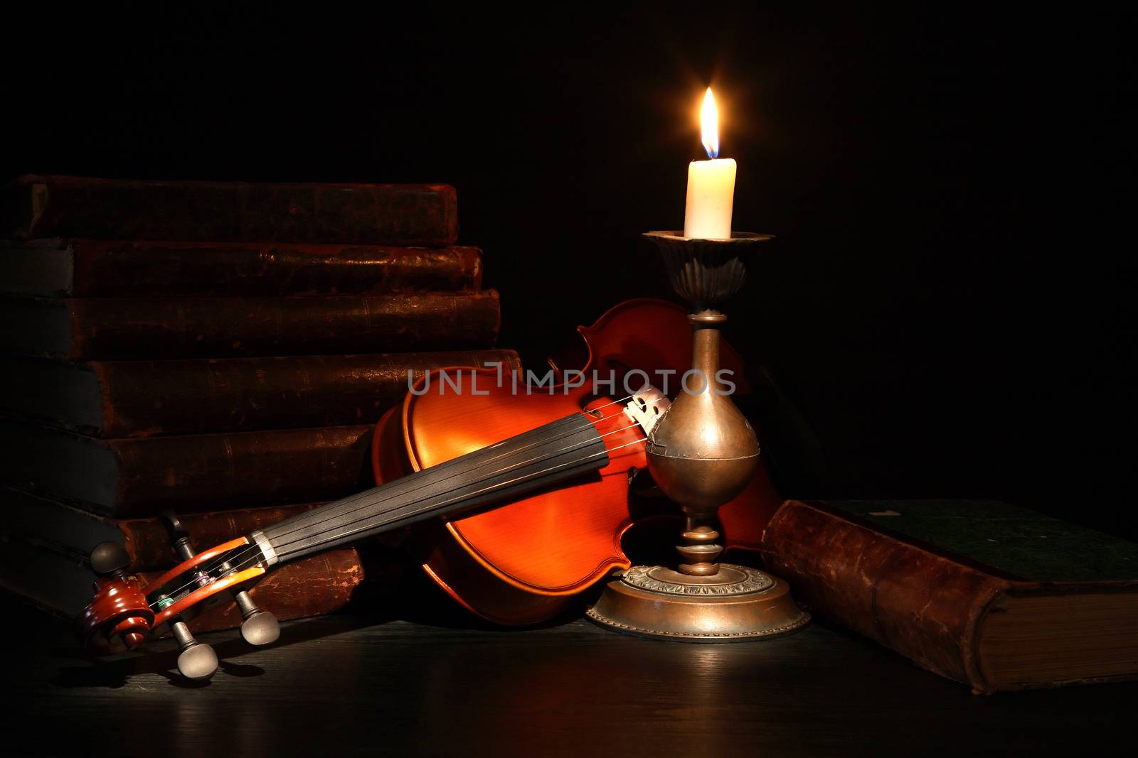 Nice violin near stack of old books and candle against black background