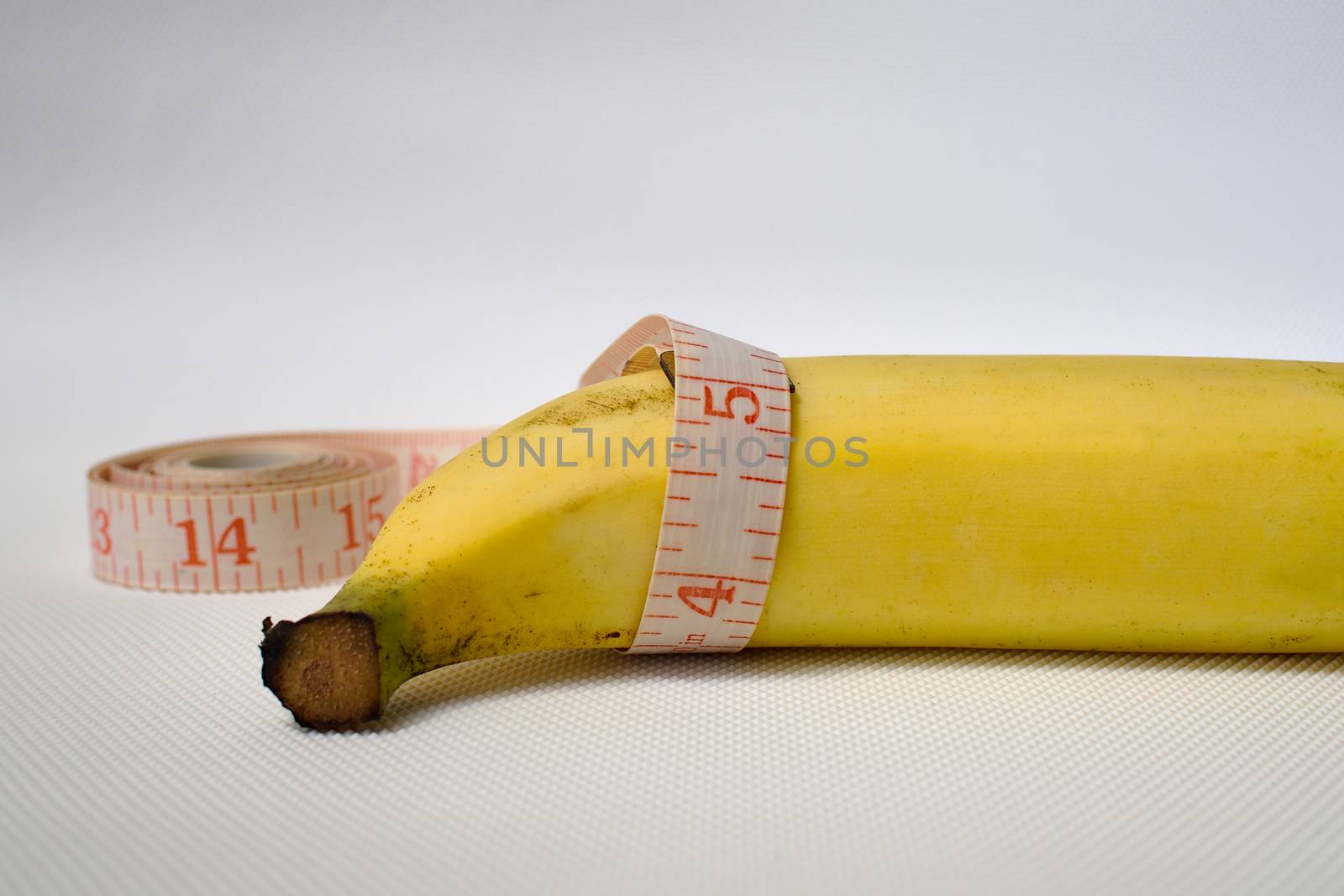 Penis size concept using ripe banana and soft measuring tape in white background by Faeldin