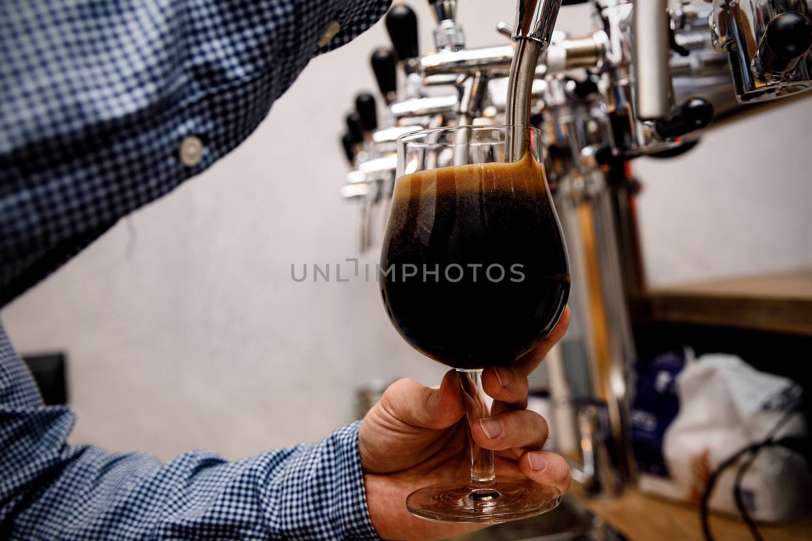 The bartender pours fresh black beer from tap in the pub