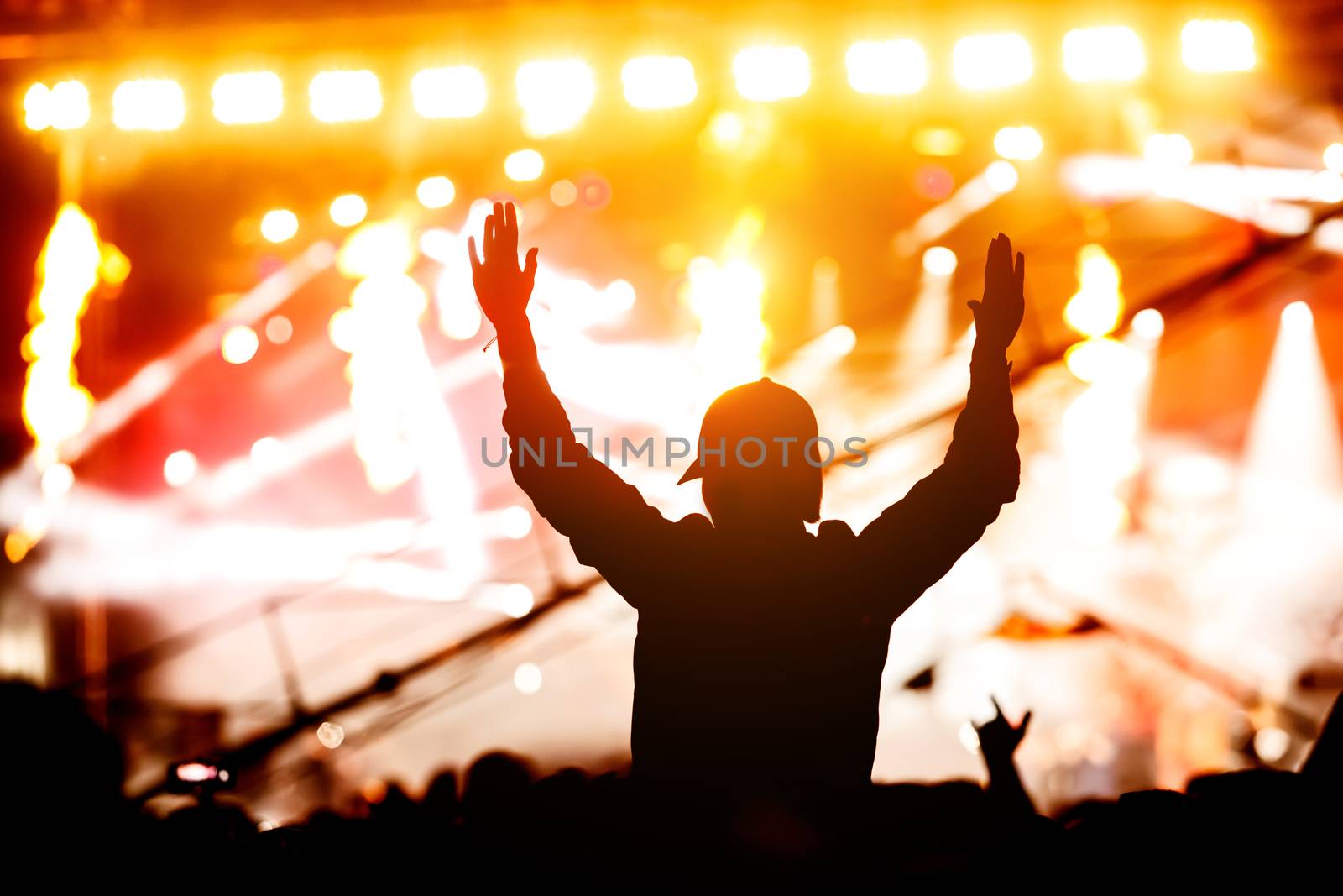 A girl silhouette with his hands up at a concert of his favorite group. Light from the stage
