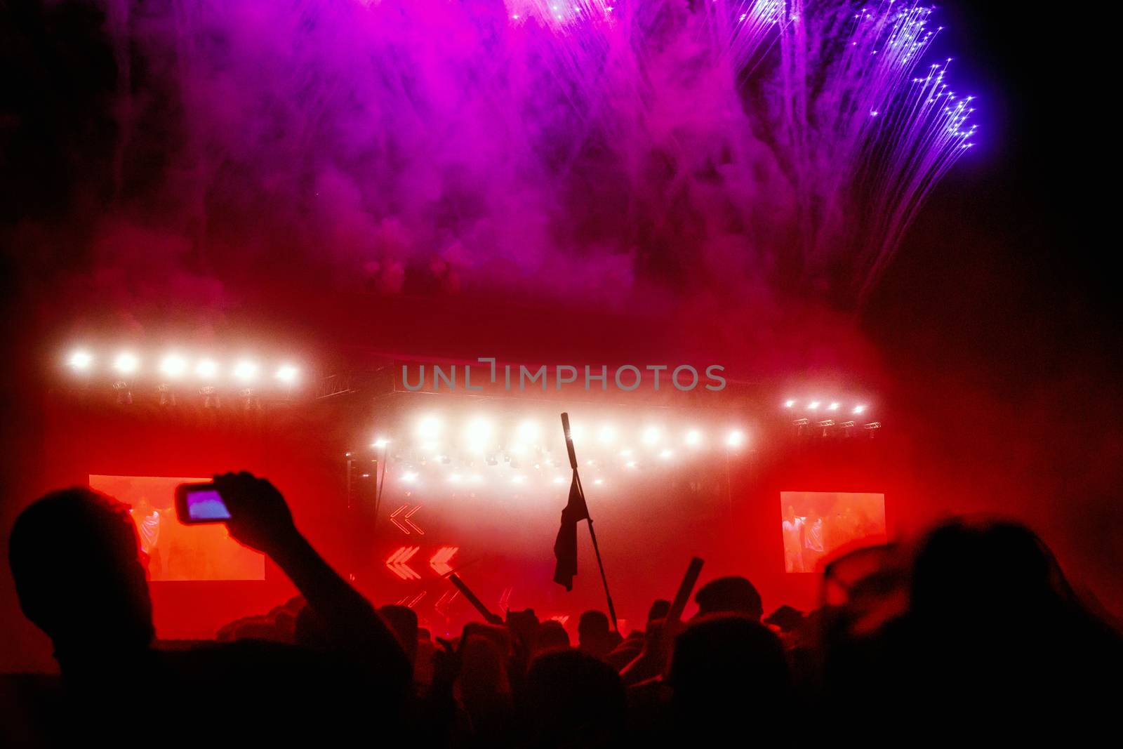 Crowd with flag around big concert stage with fire production at outdoor music festival