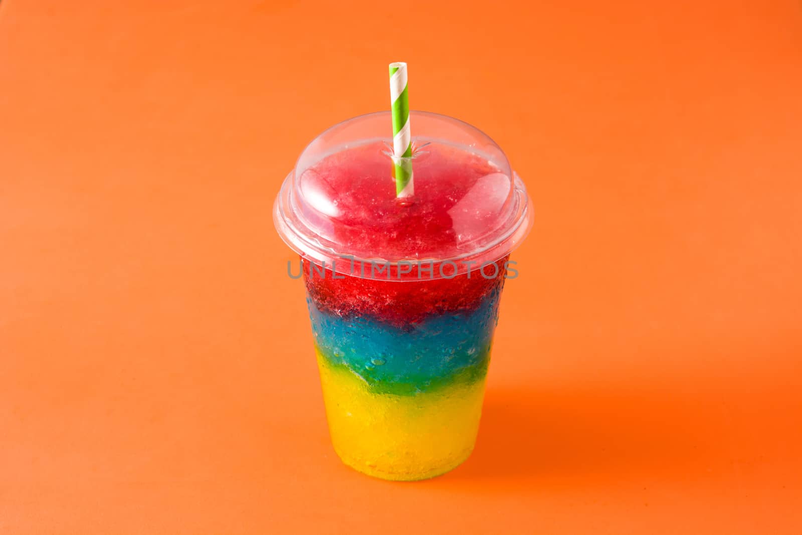 Colorful slushie of differents flavors with straw on orange background