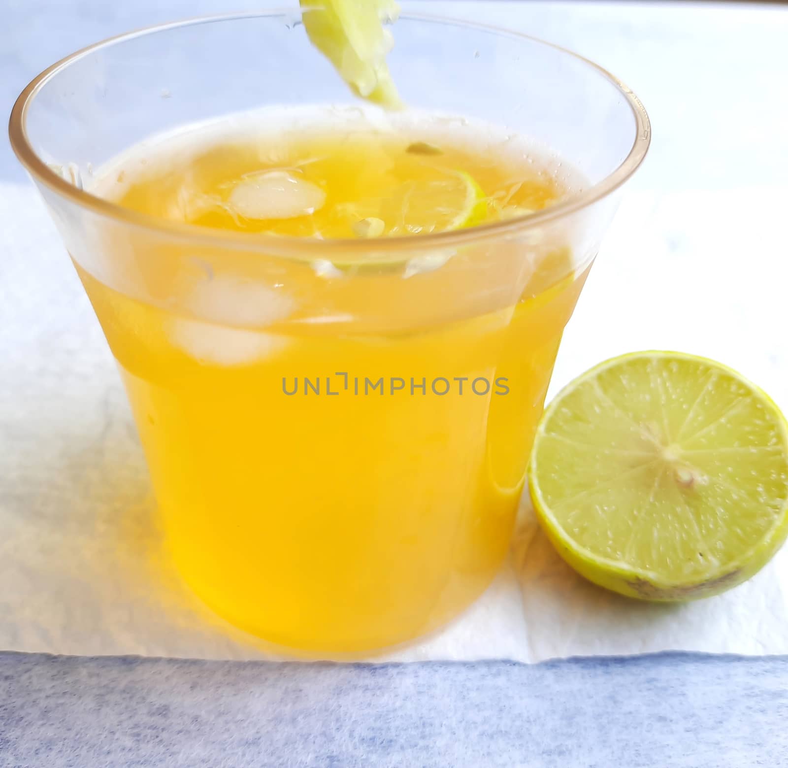 Lemon juice in glass with added orange syrup and ice cubes and half slice of lemon inside and outside of glass placed beautifully in white background by AnithaVikram