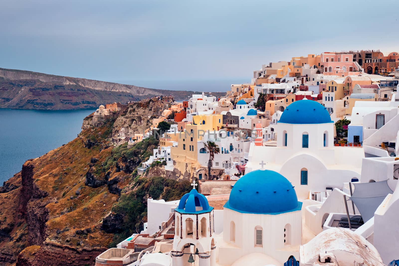 Famous greek iconic selfie spot tourist destination Oia village with traditional white houses and church in Santorini island on sunset in twilight, Greece