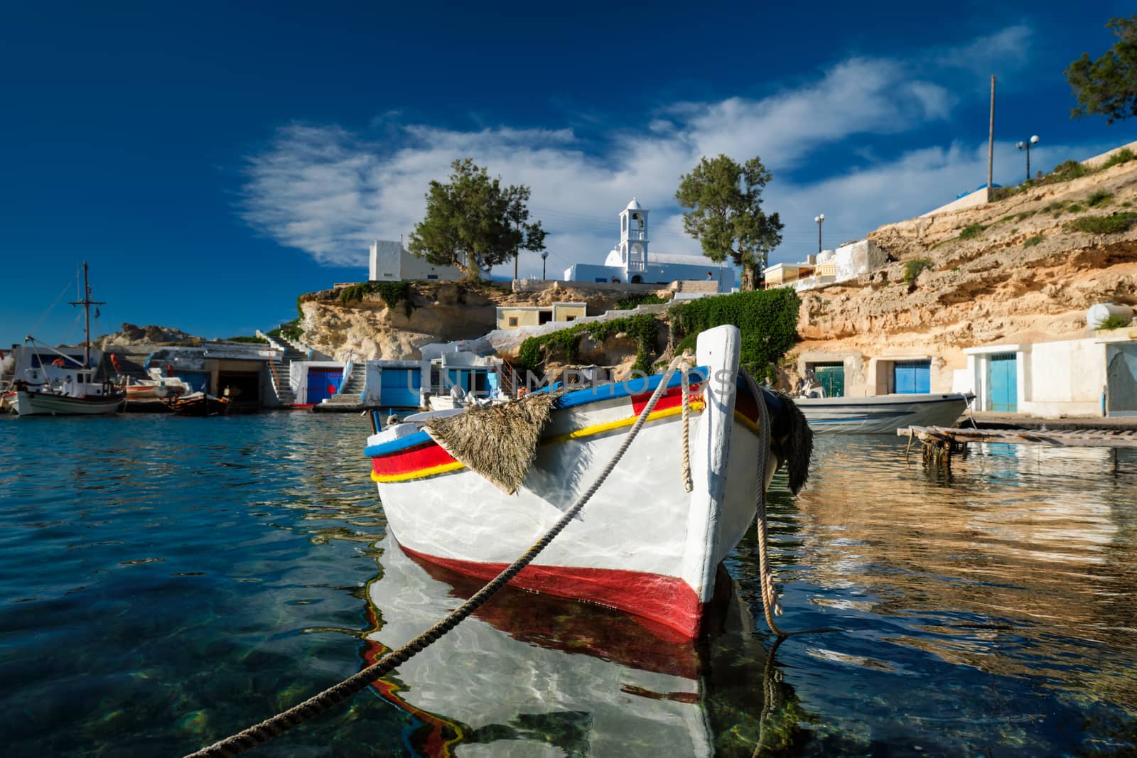 Fishing boats moored in crystal clear turquoise sea water in harbour in Greek fishing village of Mandrakia, Milos island, Greece. Horizontal camera pan