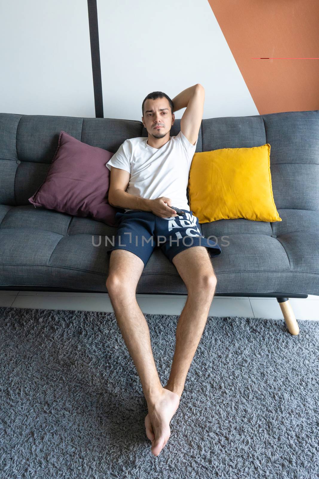 A thin guy in home clothes sits on a sofa and watches TV. Bored  by Try_my_best