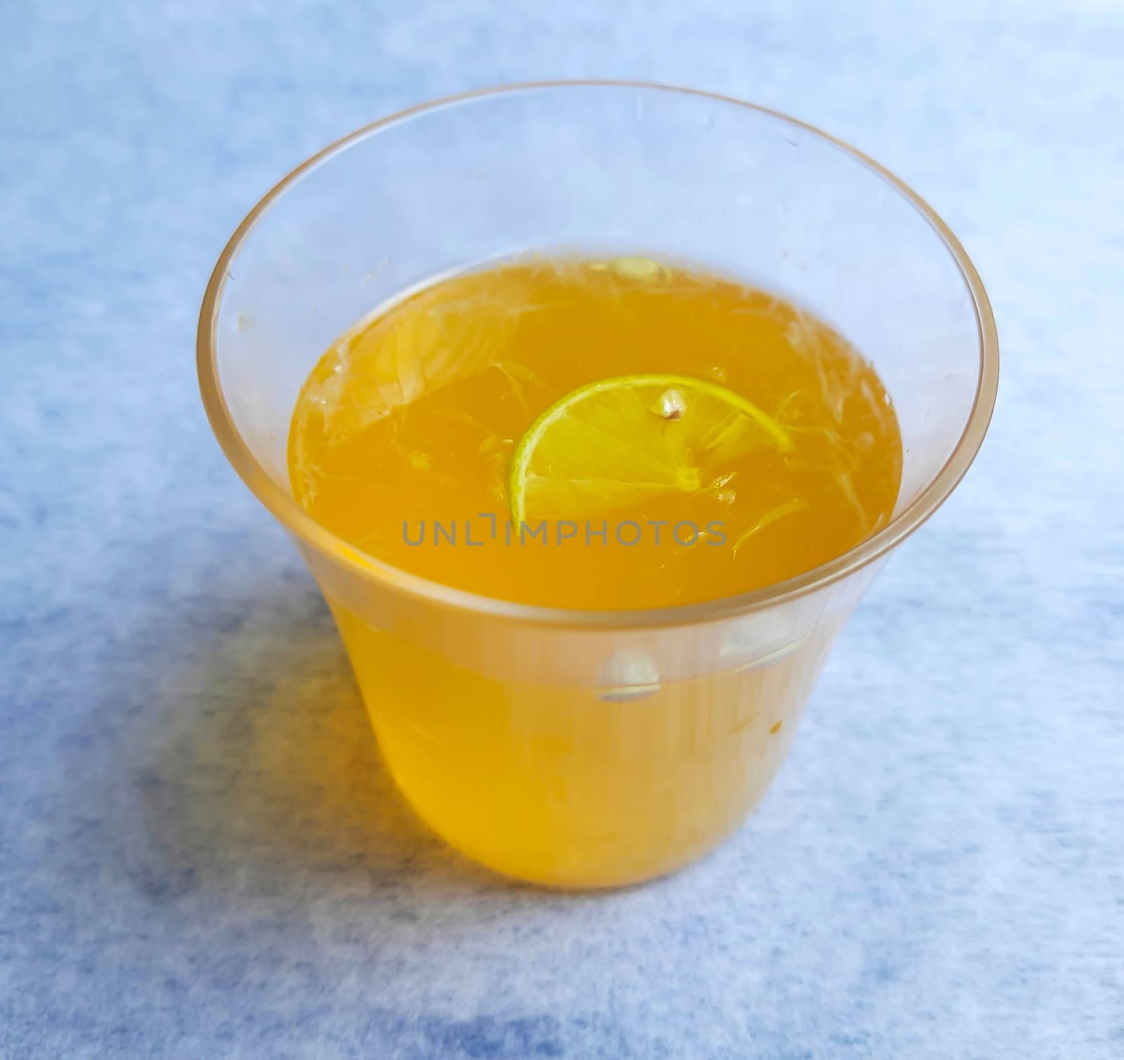 Lemon juice in glass with added orange syrup and slice of lemon inside placed beautifully in white background