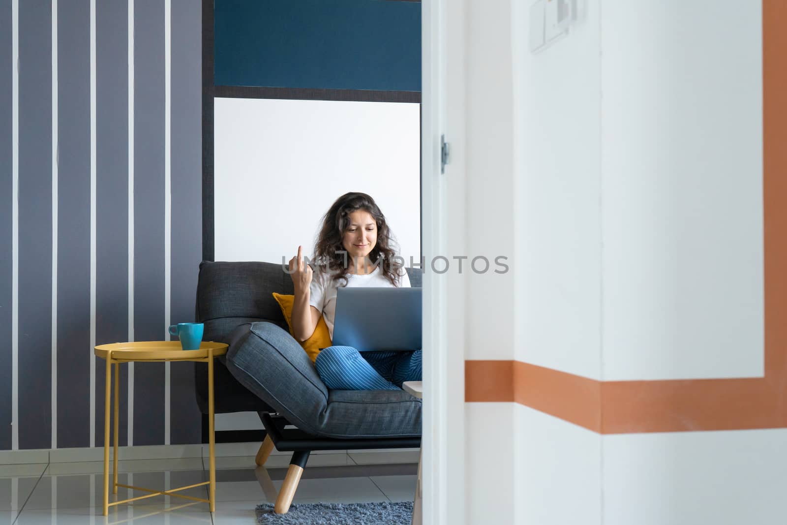 Beautiful girl sitting with a laptop on a sofa in a stylish room. Work from home. Work atmosphere in a good mood.