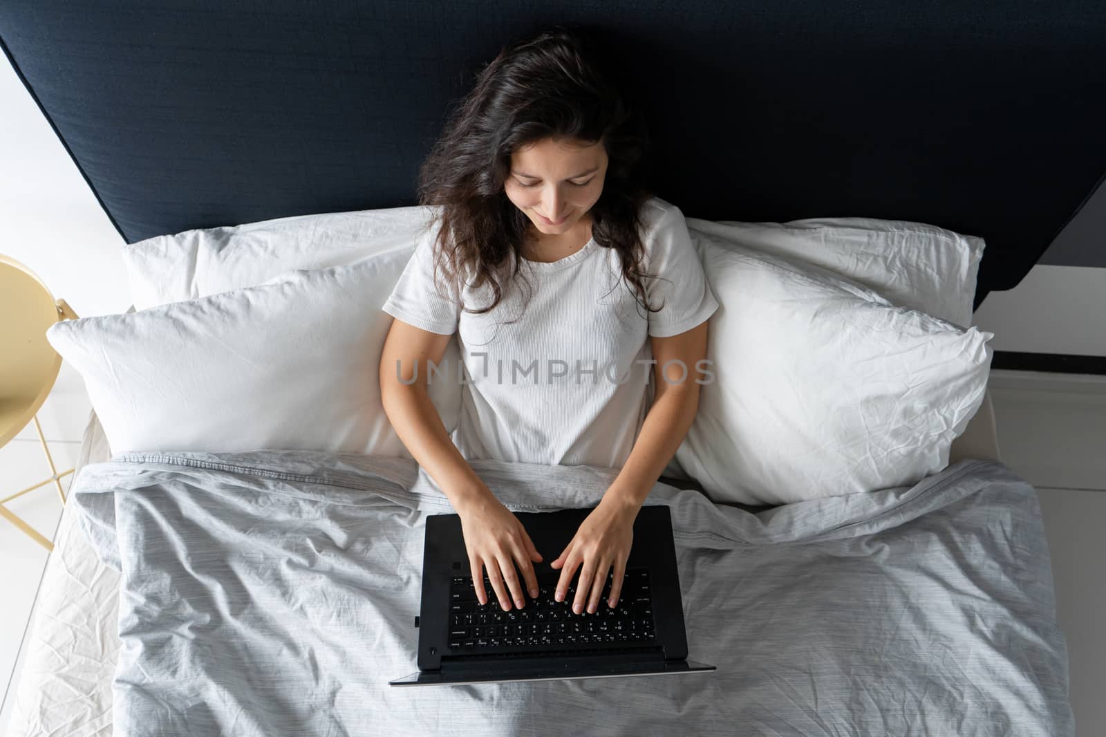 Beautiful brunette girl in bed with a laptop. Work from morning to late night. Electronic gadgets before bedtime or in the morning. by Try_my_best