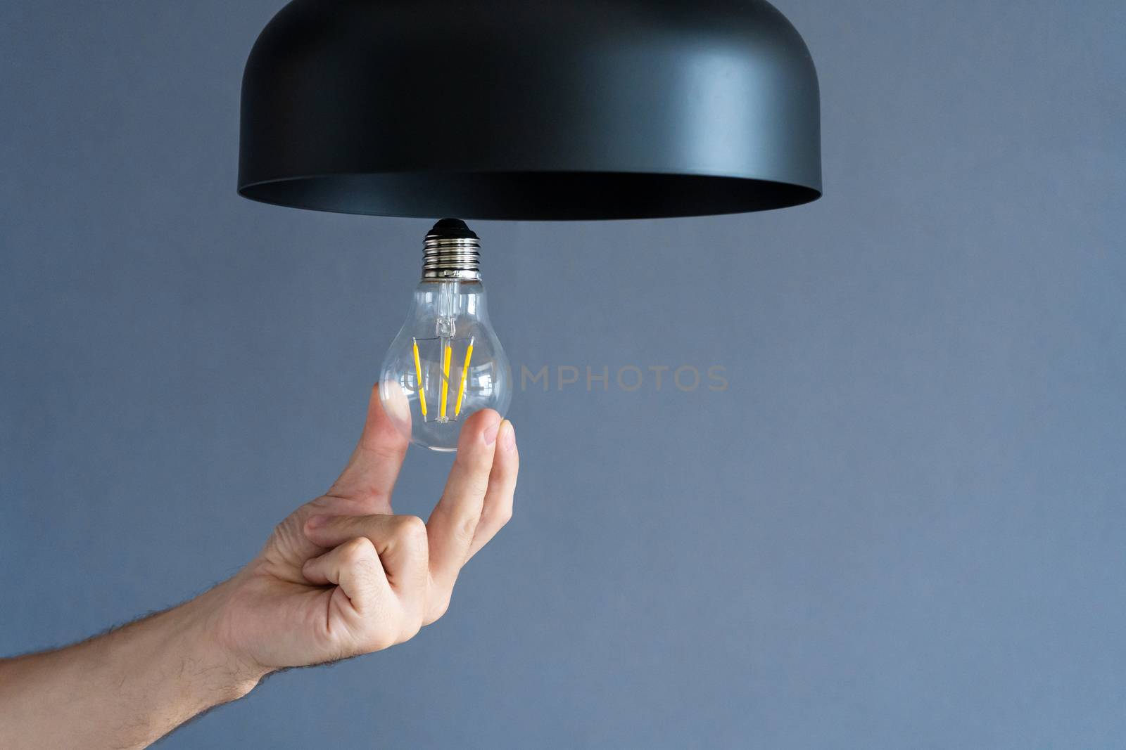 Close-up. A hand changes a light bulb in a stylish loft lamp. Spiral filament lamp. Modern interior decor