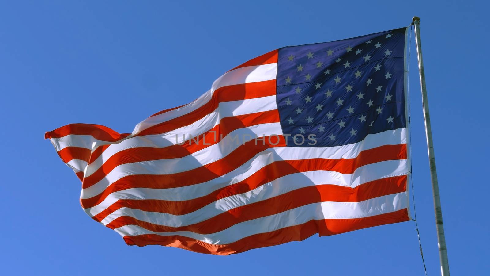 USA flag on flagpole. American flag - symbol of freedom and law in the USA. American flag flies in the sky as a symbol of the Great Country of the USA. Big American flag against blue sky.