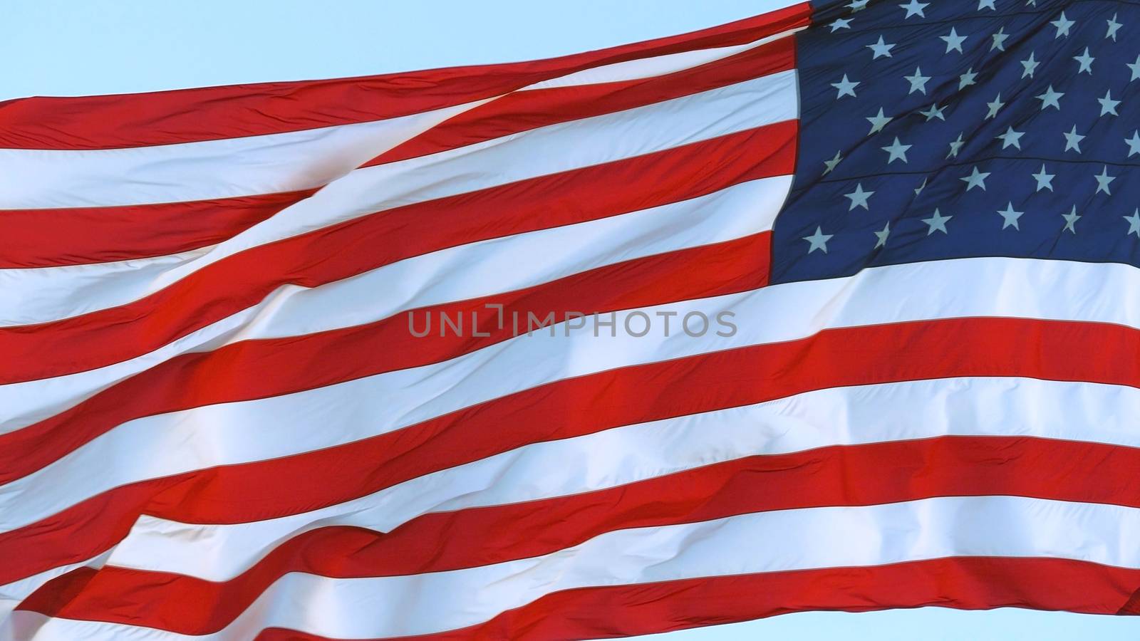 American Flag blowing in the wind with a blue sky. USA American Flag. Waving United states of America famous flag in front of blue sky. Independence Day, Labor day, Flag Day - American Celebration