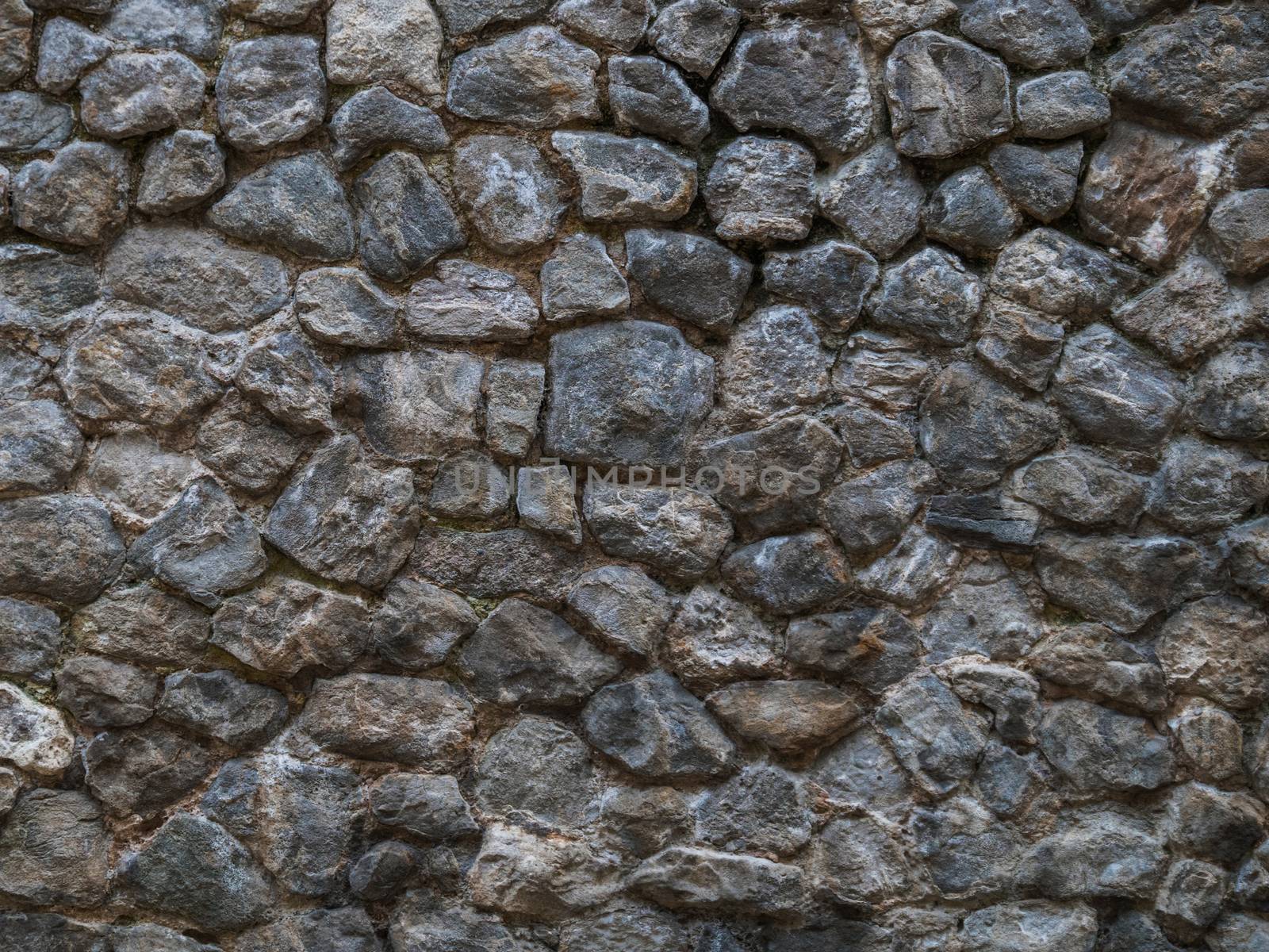 Stone wall - building feature. Background image of weathered stained old stone wall of rough stones of various shapes and sizes. Stone wall of dark rough cobblestone. Cobble stone wall texture.
