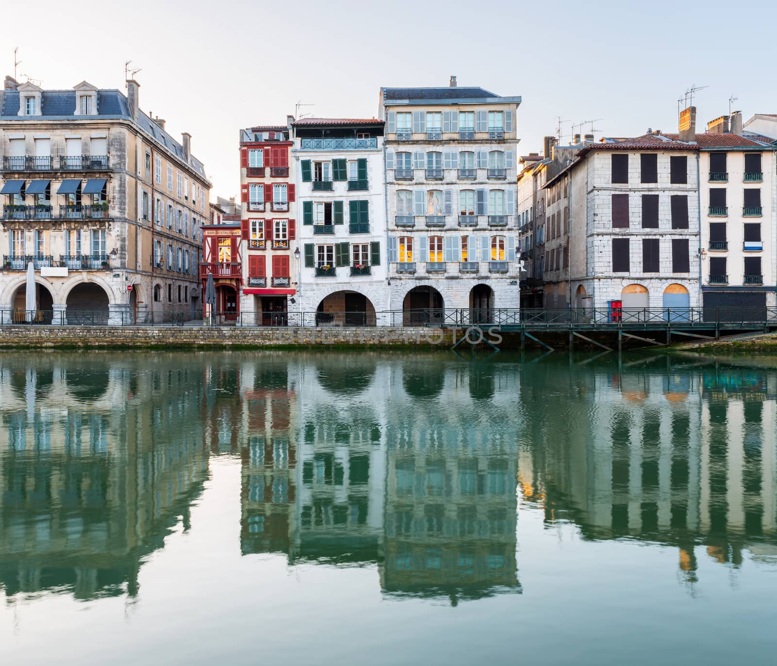 Old traditional building facades and their reflections in the Nive River at sunrise in Bayonne, France.