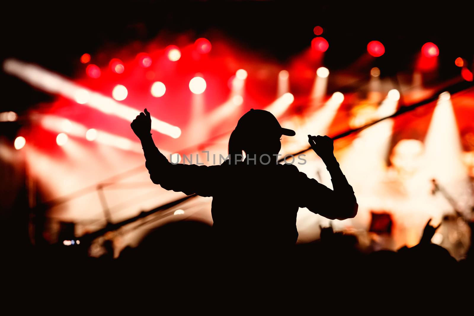 A girl silhouette with his hands up at a concert of his favorite group. Light from the stage