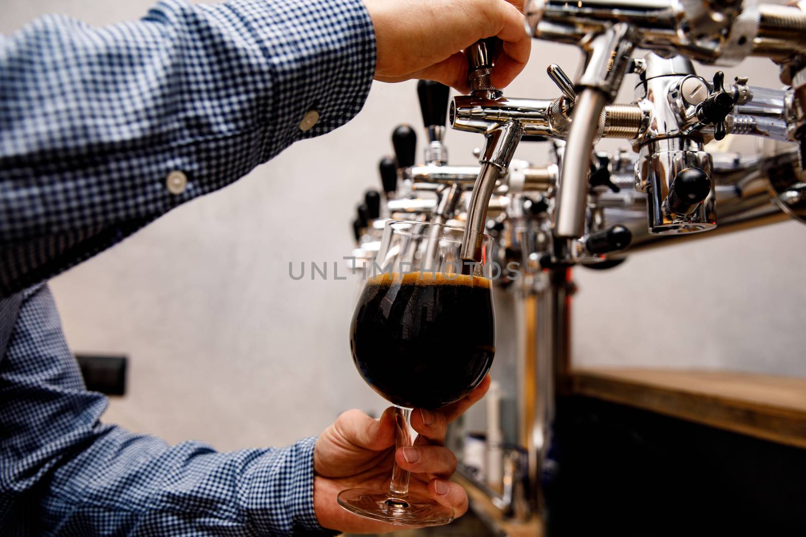 The bartender pours fresh black beer from tap in the pub