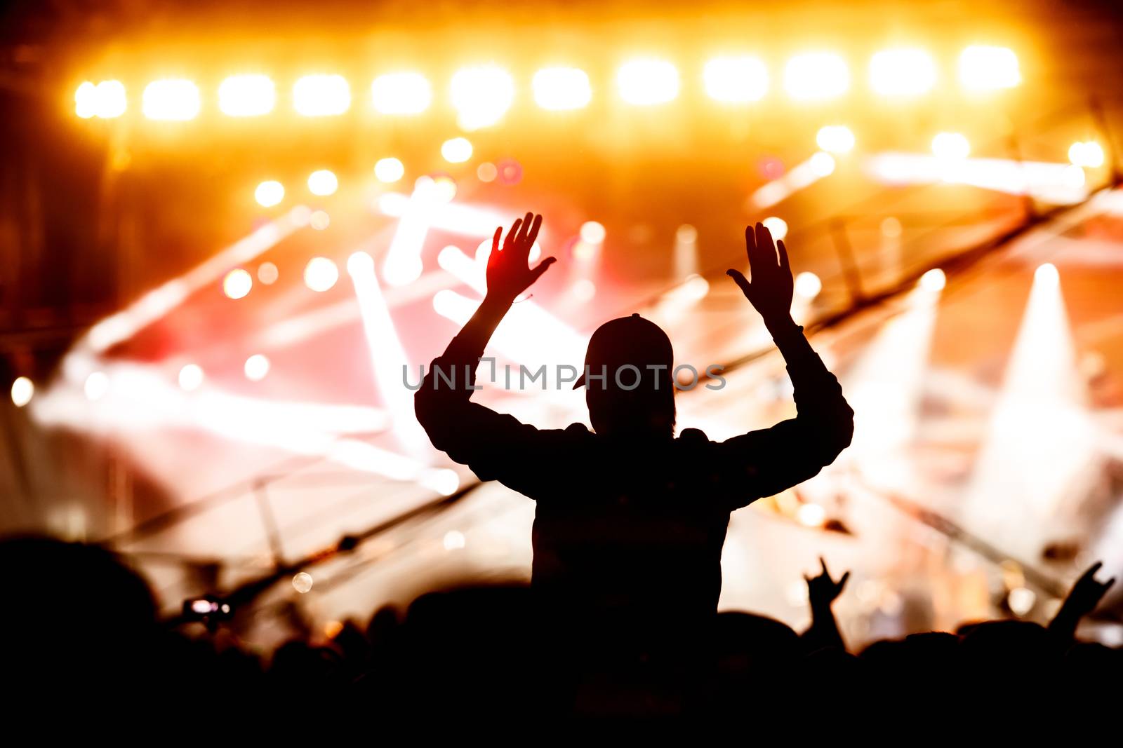 A girl silhouette with his hands up at a concert of his favorite group. Light from the stage