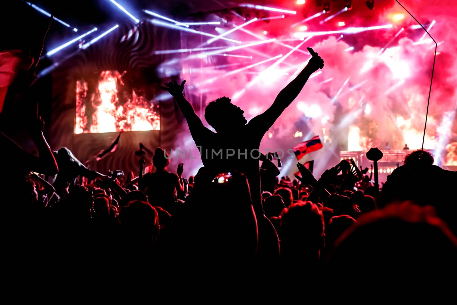 A lot of hands, crowd on concert, purple light. Man with smartphone in the center