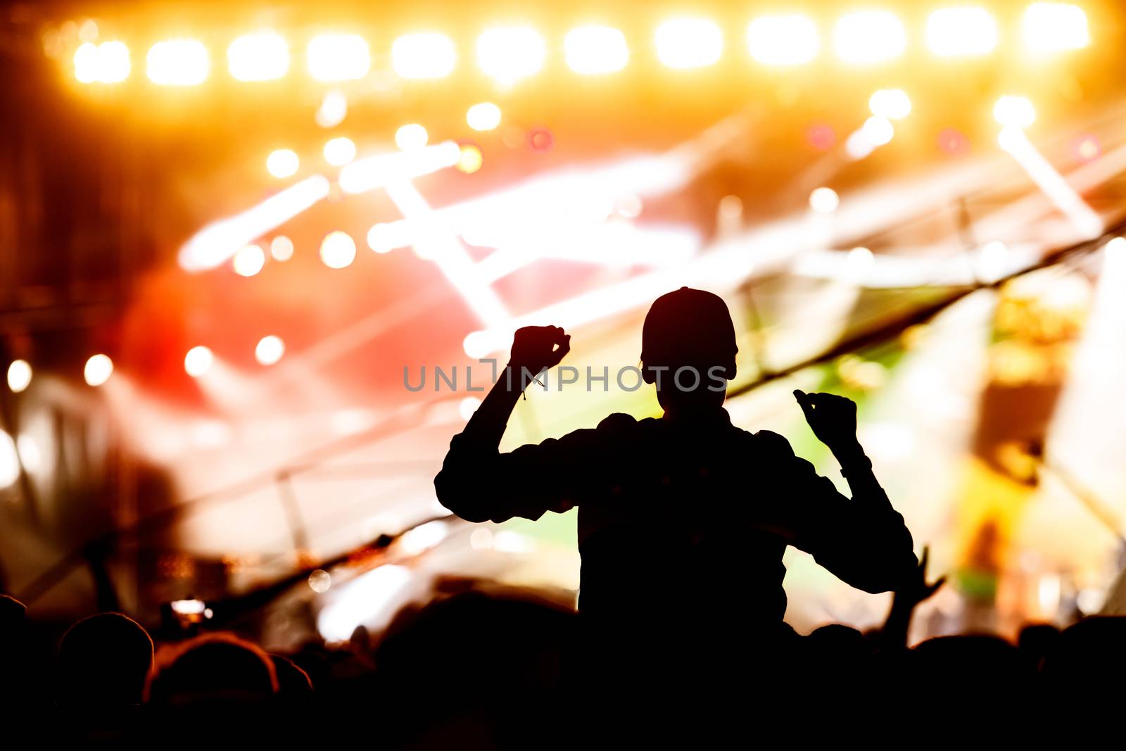 A man silhouette with his hands up at a concert of his favorite group. Light from the stage