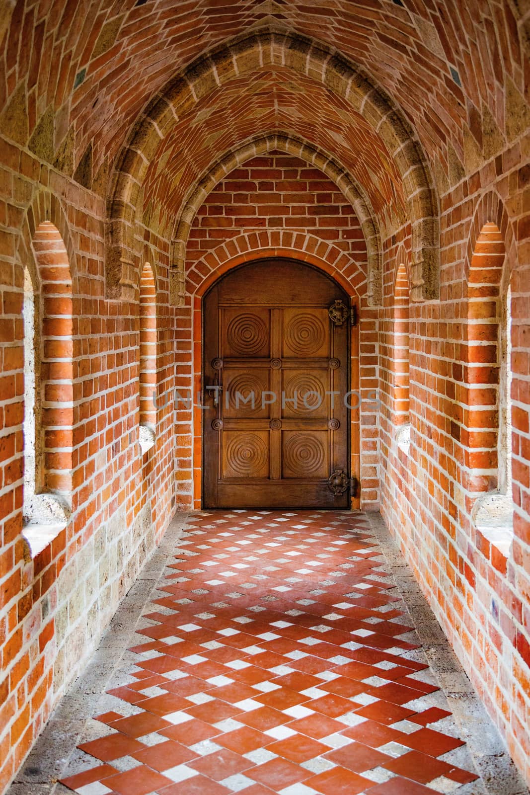 Wooden ancient door at the end of the brick corridor with arches.