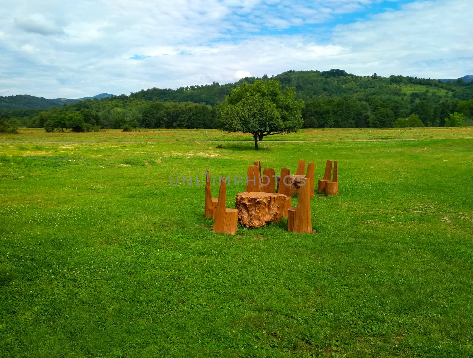 Table with solid wood chairs on a green lawn on a background of mountains, outdoor recreation. Outdoor restaurant area against the backdrop of a mountain landscape