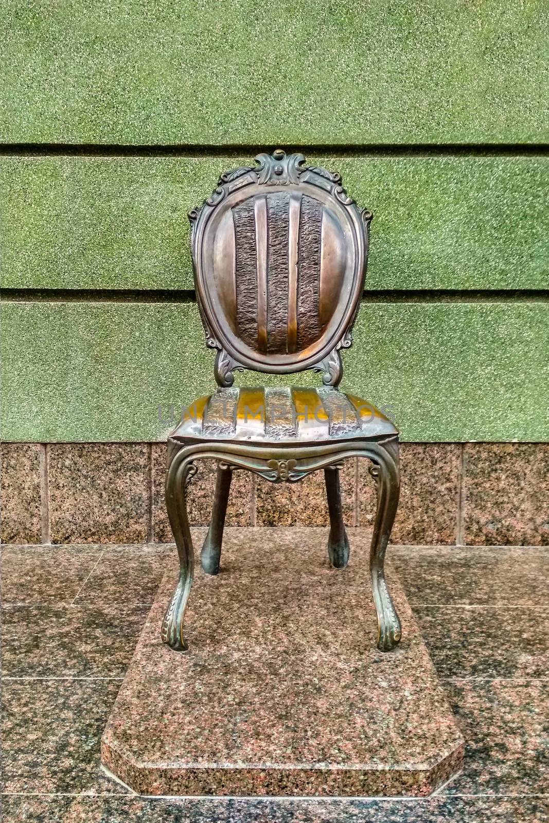 Bronze chair monument on a marble pedestal against the background at the green wall by mtx