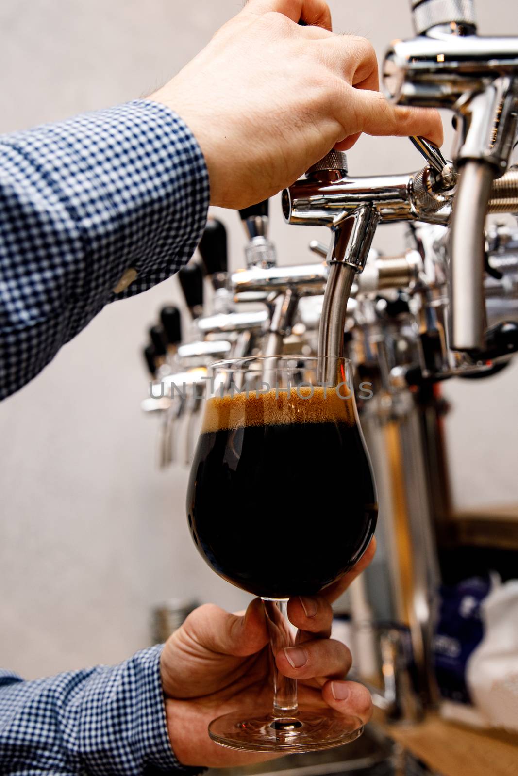 The bartender pours fresh dark beer from tap in the pub